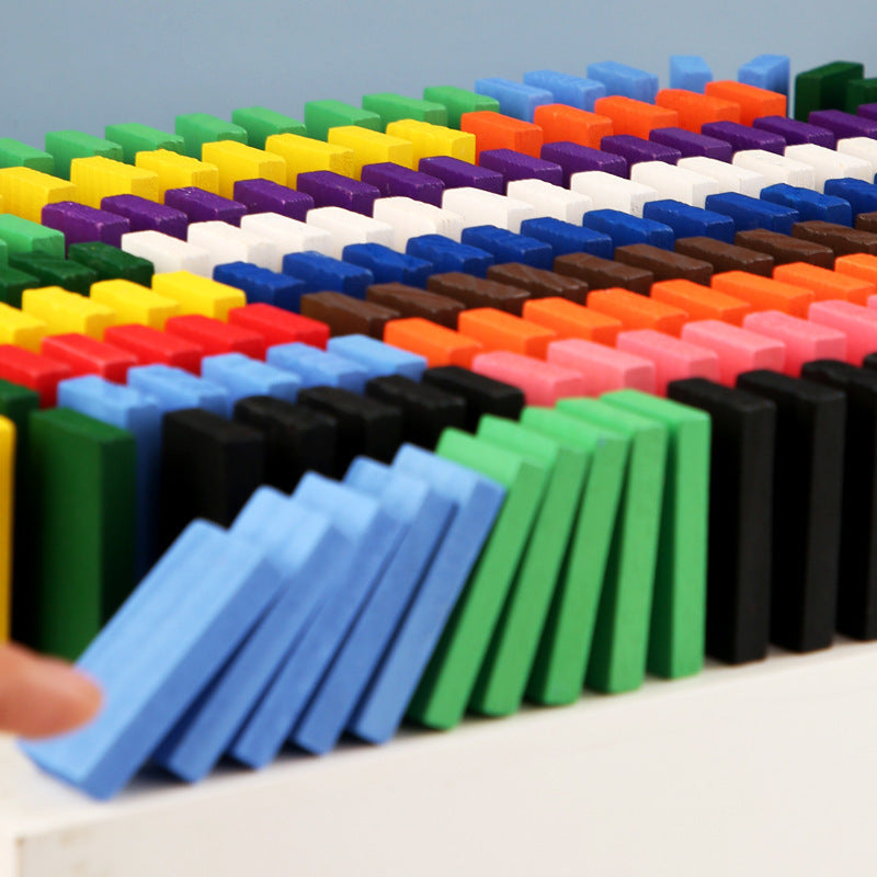 The image showcases a colorful array of wooden domino blocks arranged in neat rows on a white platform. The dominoes come in various vibrant colors, including red, yellow, green, blue, purple, black, and white. Additionally, there are small structures built with the dominoes and other wooden pieces, adding an element of creativity and construction to the play. This setup is visually appealing and highlights the potential for imaginative and educational play with the domino blocks.