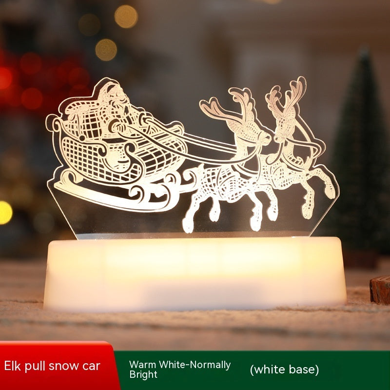 Illuminated Christmas LED lamps with a 'Merry Christmas' sign featuring reindeer antlers and a Christmas tree with presents underneath. The lamps glow warmly, set against a backdrop of a decorated Christmas tree with lights and ornaments. Pine branches and a pine cone add to the festive ambiance.