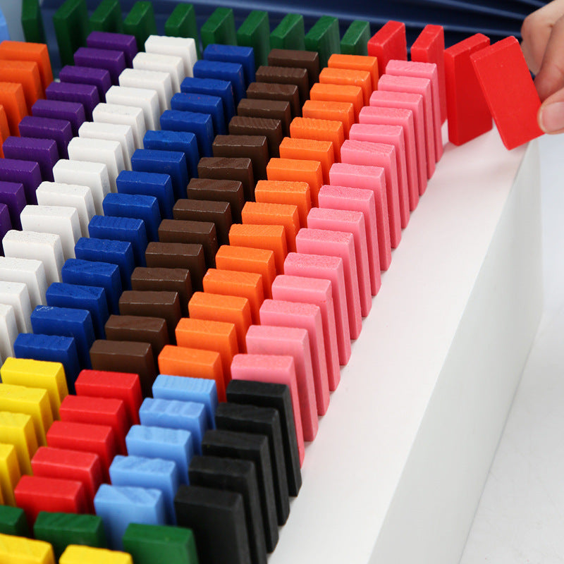 The image showcases a colorful array of wooden domino blocks arranged in neat rows on a white platform. The dominoes come in various vibrant colors, including red, yellow, green, blue, purple, black, and white. Additionally, there are small structures built with the dominoes and other wooden pieces, adding an element of creativity and construction to the play. This setup is visually appealing and highlights the potential for imaginative and educational play with the domino blocks.