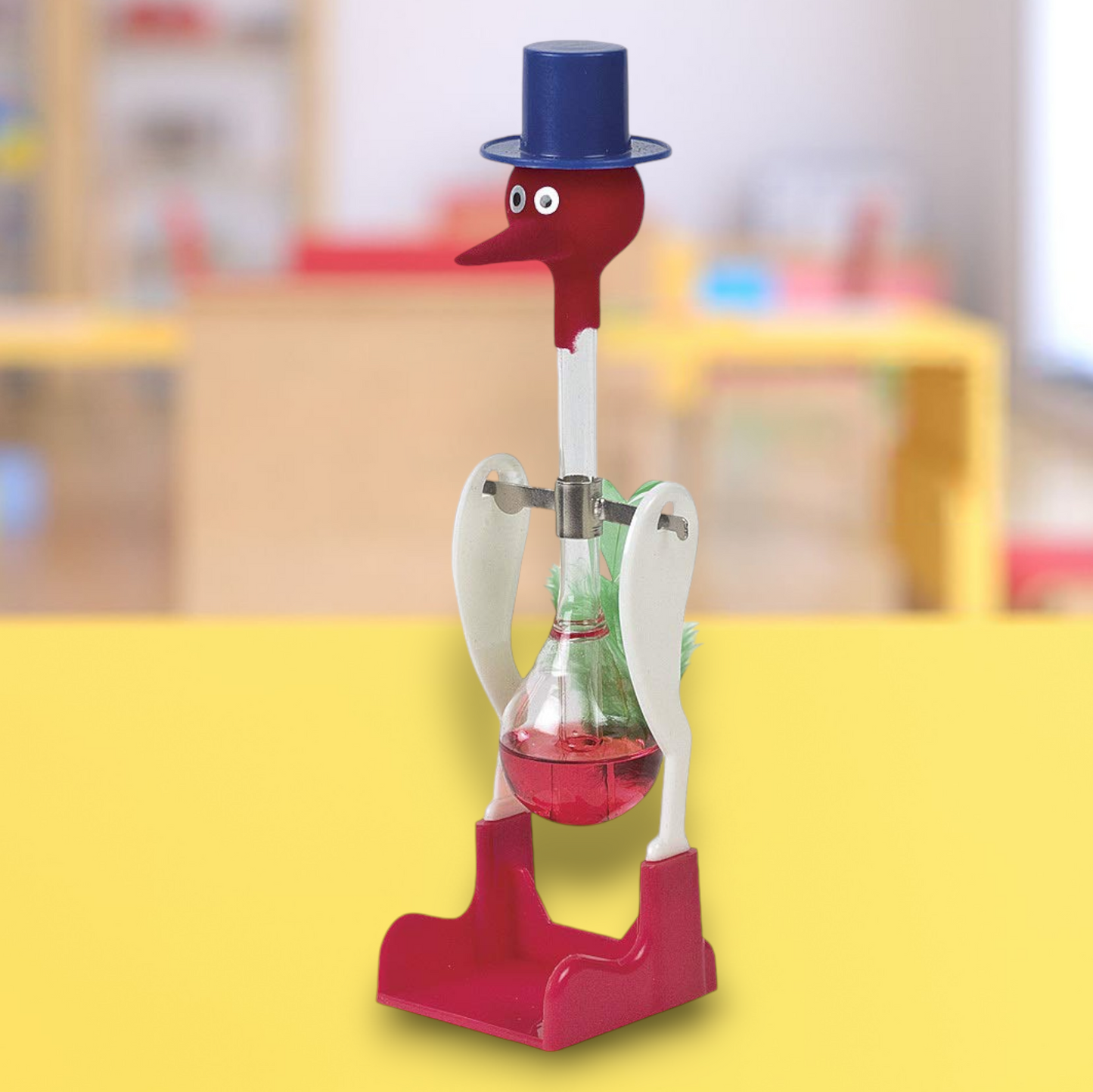 Original Drinking Bird toy featuring a red and white color scheme with a blue top hat. The bird has a clear glass tube body filled with a red liquid, which dips into the beak when activated. The base and head of the bird are red, while the midsection is white, creating a striking contrast. This classic novelty item is both amusing and fascinating to observe as it perpetually ‘drinks’ from a cup when set up properly.