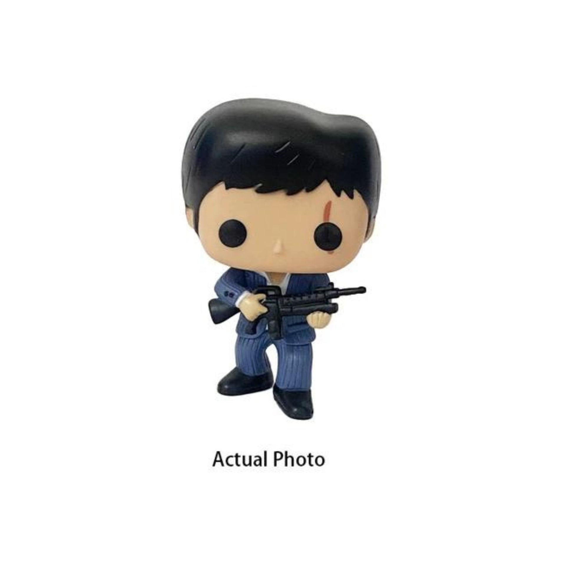 The image shows a Funko Pop! vinyl figure of Tony Montana from the movie "Scarface." The figure is dressed in a blue suit and is holding a rifle. The packaging is also visible, featuring the Pop! Movies logo, the name "Scarface," and the number 86. This collectible is part of the POP Movie Series and is designed for children aged 17 and up. The figure is highly detailed and captures the essence of the iconic character, making it an interesting and relevant item for collectors and fans of the movie.